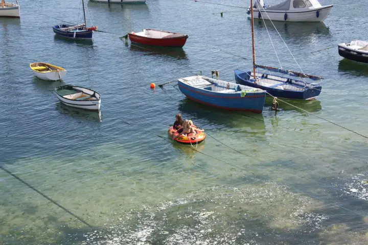Kinder paddeln im Hafen von Mousehole in einem Schlauchboot