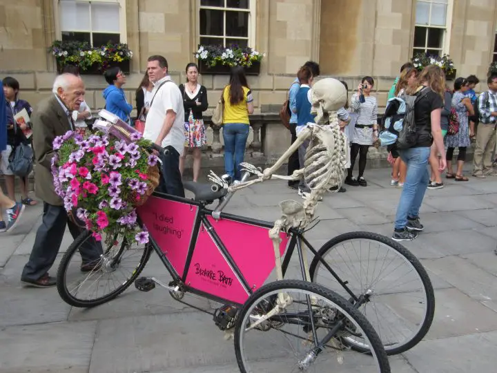 Ein Skelett auf einem Fahrrad macht Werbung für einen Stadtrundgang - und das direkt vor der Kathedrale von Bath