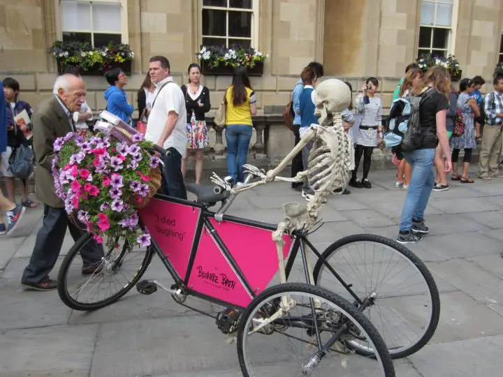 Bath, England, Cathedral Ein Skelett auf einem Fahrrad macht Werbung für einen Stadtrundgang - und das direkt vor der Kathedrale von Bath